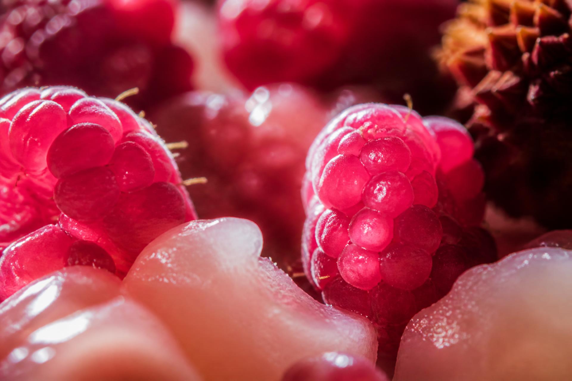 Close-up of raspberries, peeled litchi and rose petals on ceramic